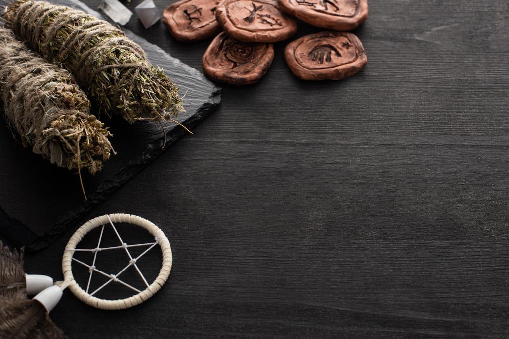 Palos de manchas de hierbas, atrapasueños y amuletos de arcilla sobre fondo de madera oscura
 - Foto, imagen