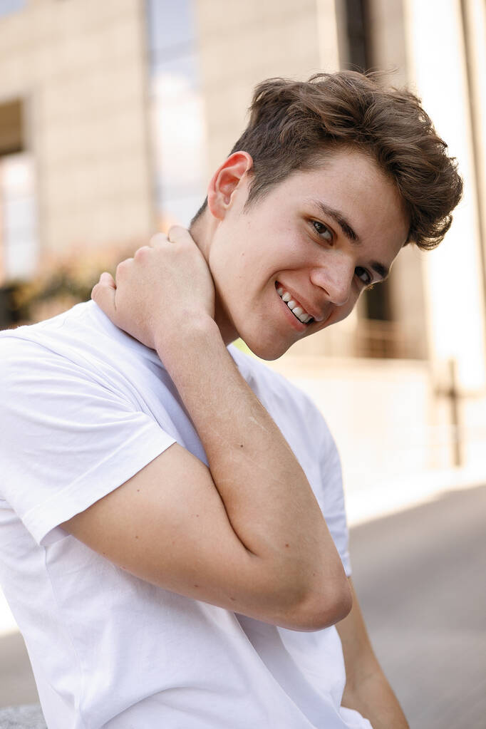 Elegáns fiatalember mosolyog egy divatos fekete ing egy fehér elegáns póló fekete nadrág egy divatos frizura nyugszik, közel egy modern üzleti központ. közelkép portré - Fotó, kép
