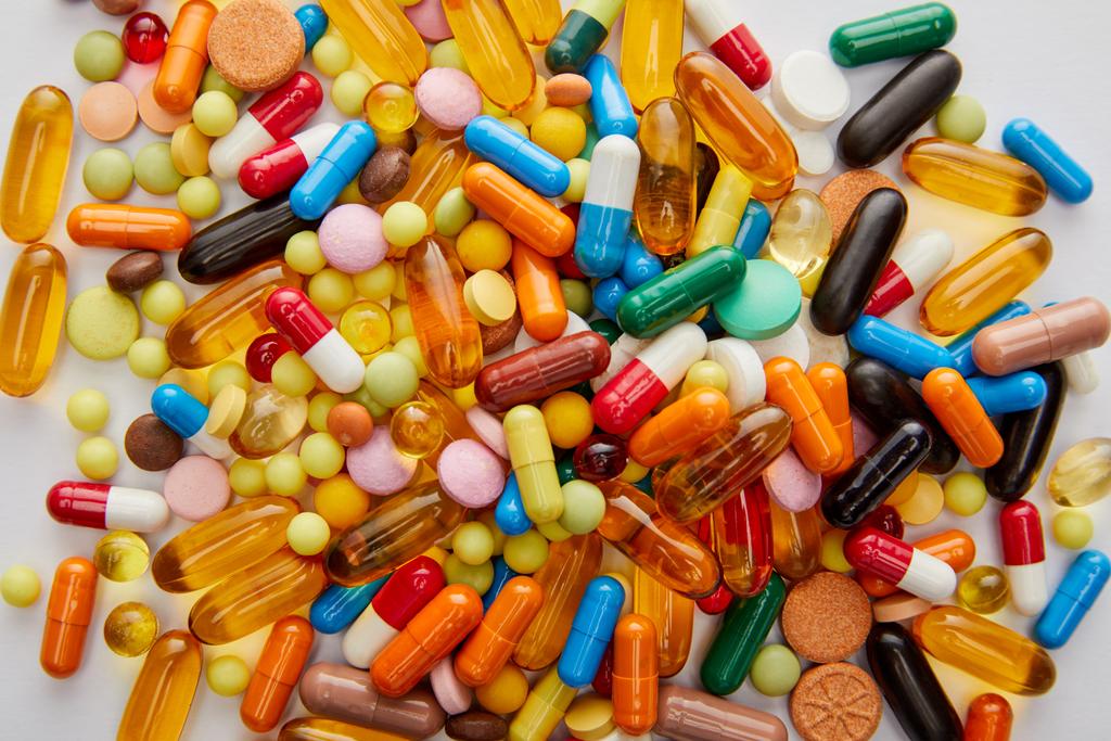 Bovenaanzicht van heldere capsules en pillen op witte achtergrond - Foto, afbeelding