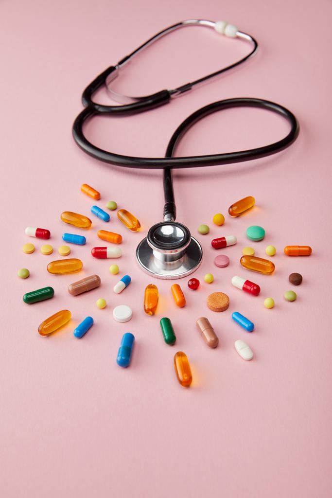 High angle view of stethoscope near bright colorful pills on pink background - Photo, Image