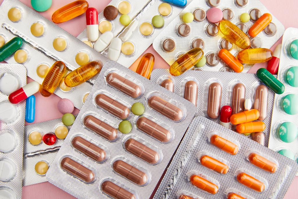 Вид сверху цветных капсул и таблеток на розовом фоне
 - Фото, изображение
