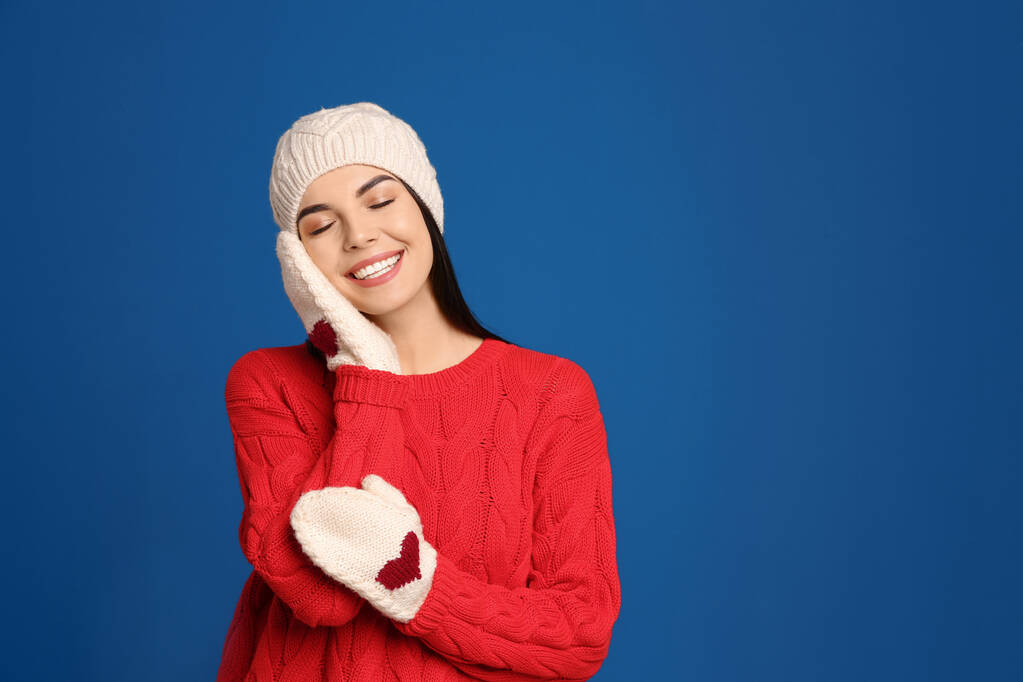 Mavi arka planda kalın kazak, eldiven ve şapka giyen genç bir kadın. Kış mevsimi - Fotoğraf, Görsel