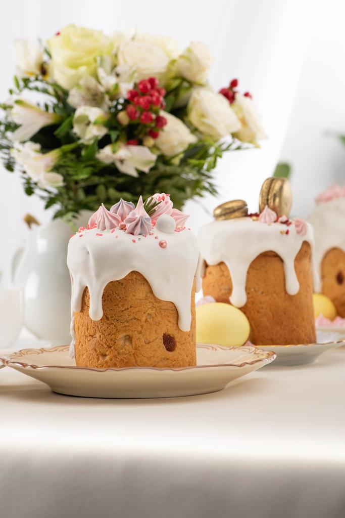 selective focus of delicious easter cakes with golden french macaroons and meringue on icing near floral bouquet - Photo, Image