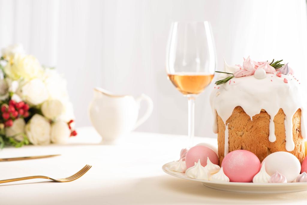 selective focus of delicious Easter cake decorated with meringue with pink and white eggs on plate near wine glass and flowers - Photo, Image