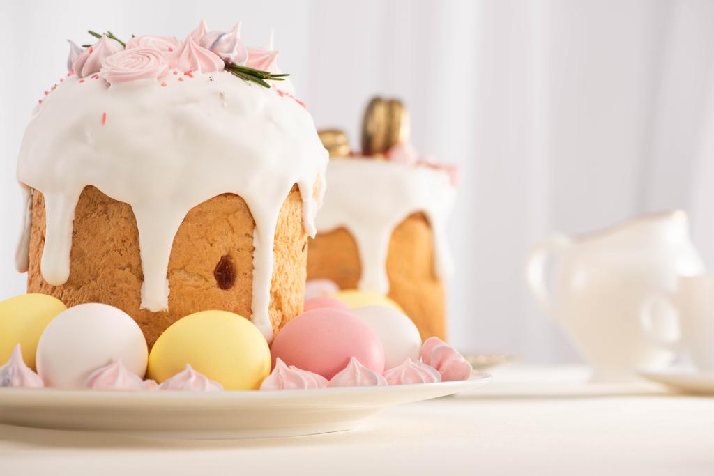 プレート上のカラフルな卵の近くにメレンゲで飾られたおいしいイースターケーキの選択的な焦点 - 写真・画像