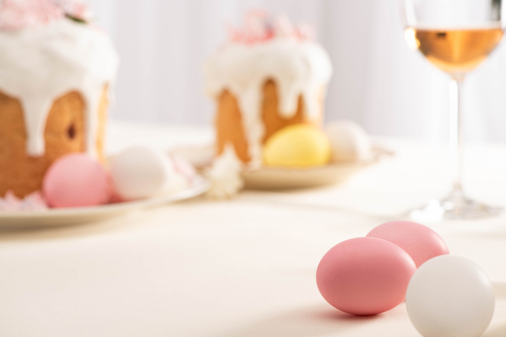 szelektív fókusz ízletes húsvéti sütemények habcsók és színes tojás tányérok közelében borospohár - Fotó, kép