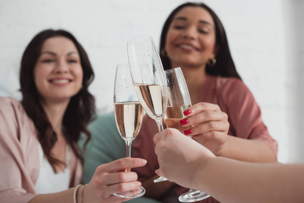 Vista cortada de mulheres africanas americanas e caucasianas sorrindo e clinking com taças de champanhe no quarto
 - Foto, Imagem