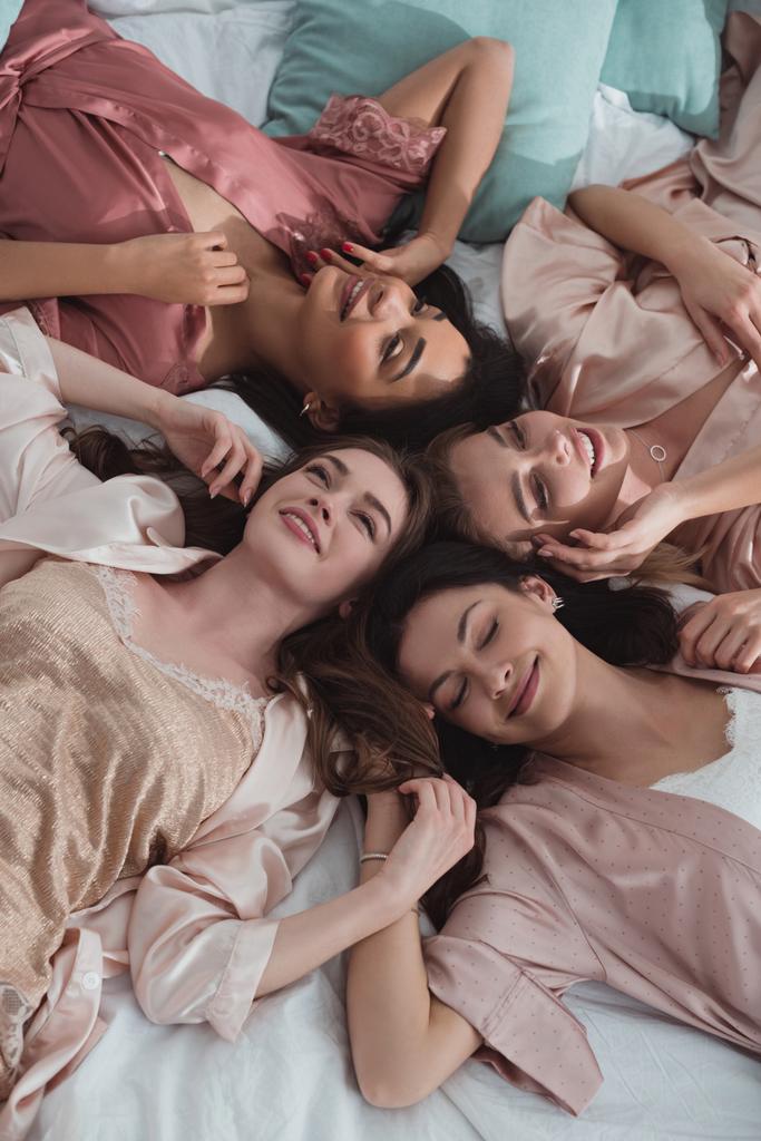 Vista superior de mujeres multiétnicas sonriendo y descansando en la cama en la despedida de soltera
 - Foto, imagen
