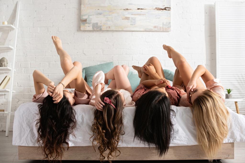 Donne multiculturali con le gambe incrociate sdraiate sul letto all'addio al nubilato
 - Foto, immagini