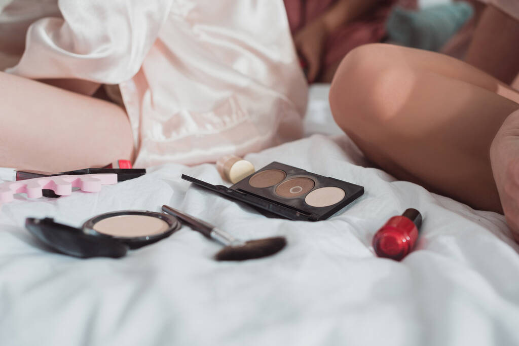 Vista ritagliata di donne vicino a cosmetici sul letto
 - Foto, immagini