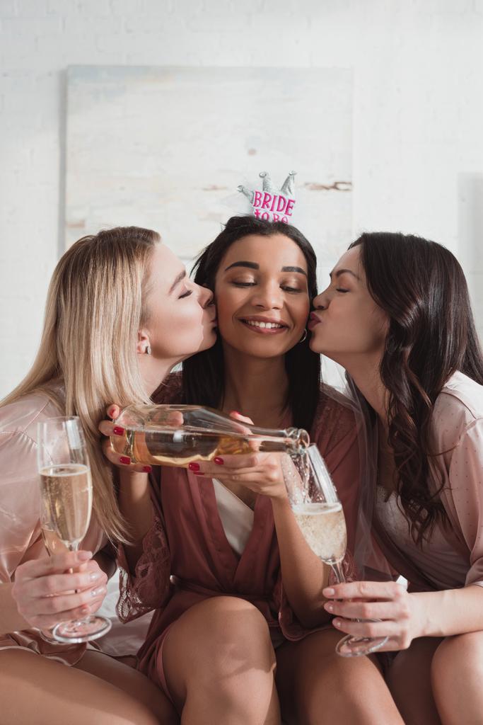 Afro-Amerikaanse bruid gieten champagne in glazen en het krijgen van kussen van vrienden op vrijgezellenfeest - Foto, afbeelding