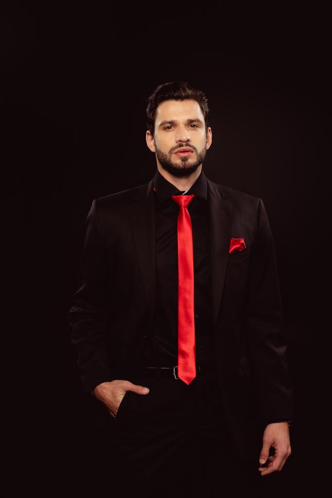 Hombre guapo en traje y corbata roja mirando a la cámara aislada en negro
 - Foto, imagen