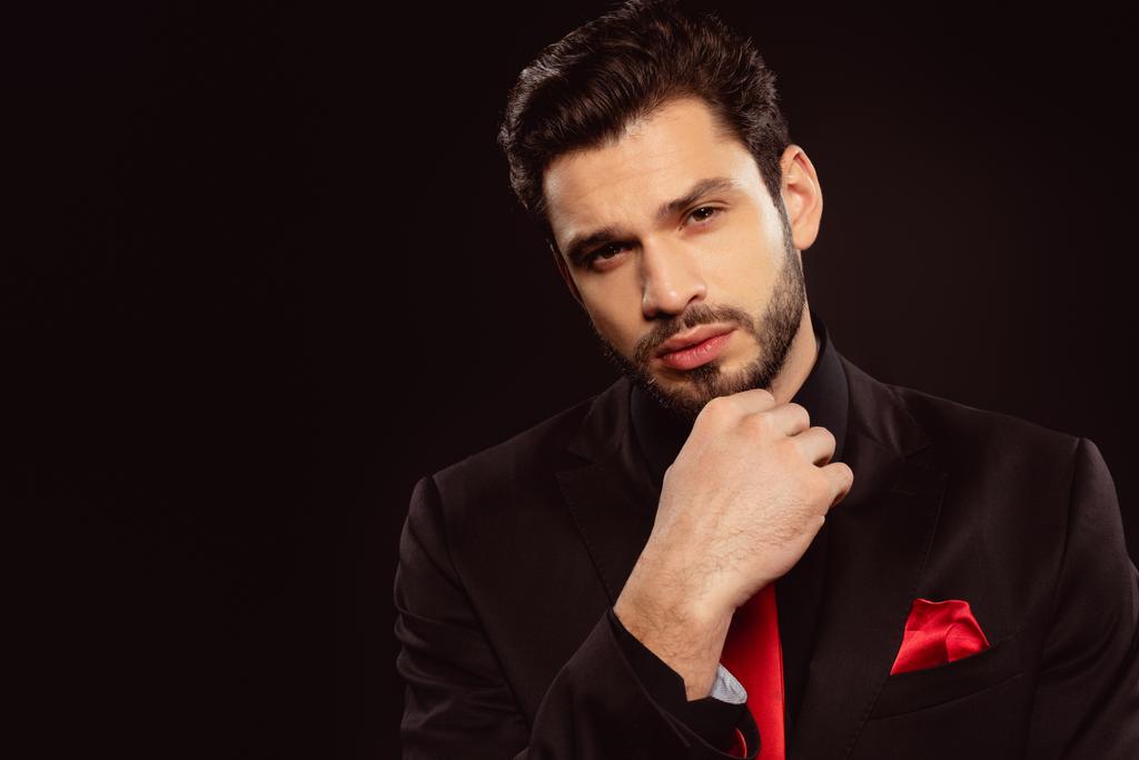 Eleganter Mann im Anzug und roter Krawatte blickt vereinzelt in die Kamera auf Schwarz - Foto, Bild