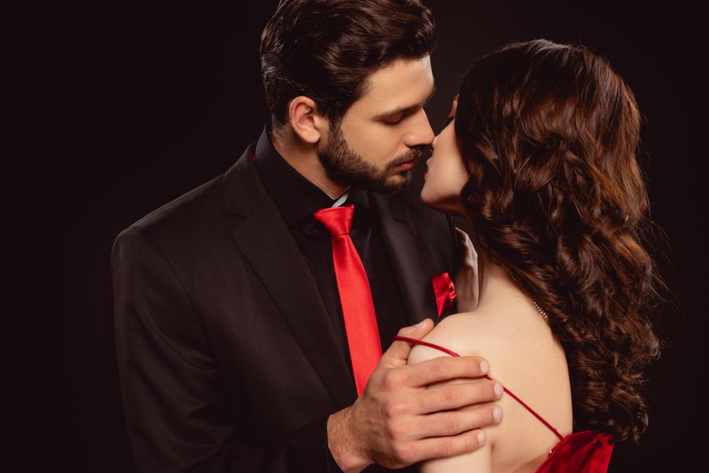 Eleganter Mann küsst Freundin beim Ausziehen Kleid isoliert auf schwarz - Foto, Bild