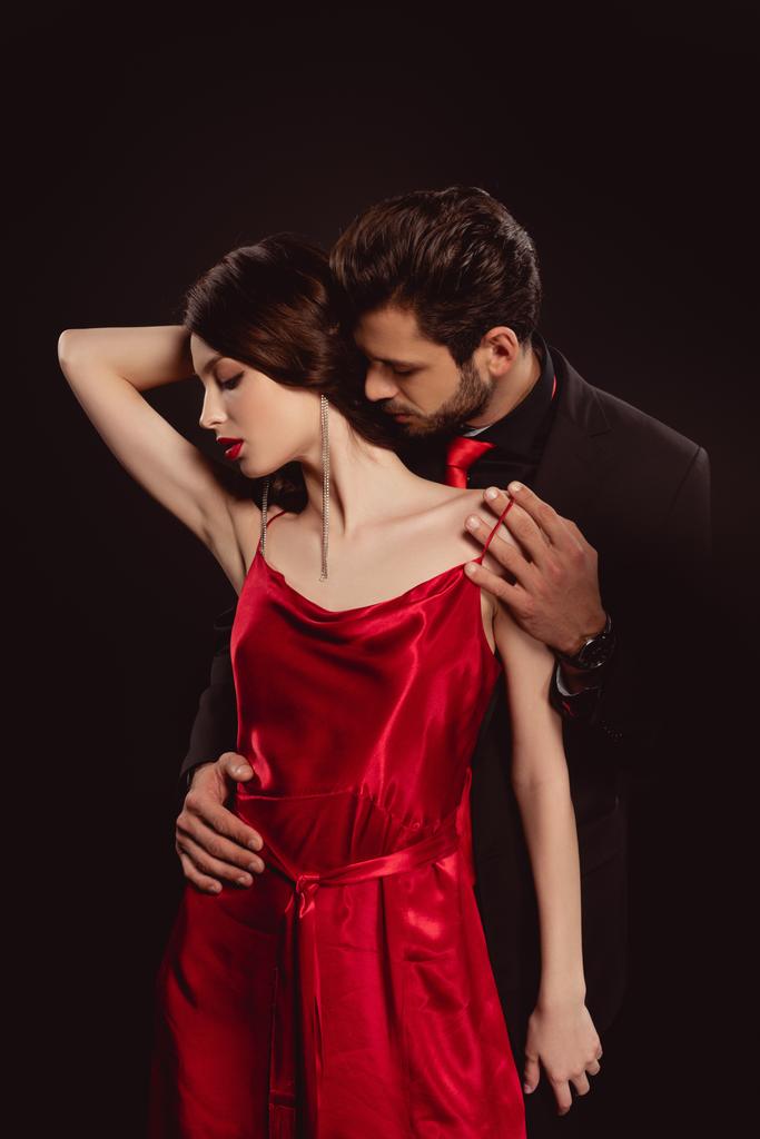 Hombre guapo abrazando y quitando vestido rojo de mujer hermosa aislado en negro
 - Foto, Imagen