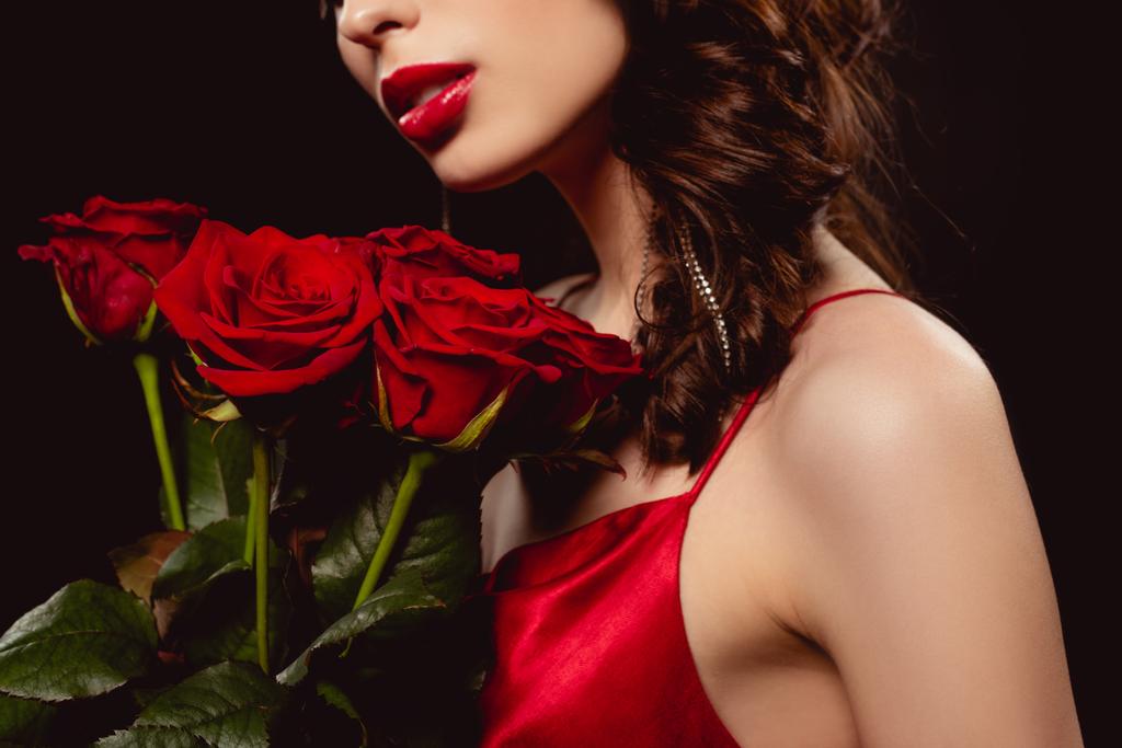 Περικοπή άποψη της κομψής γυναίκας με κόκκινα χείλη κρατώντας μπουκέτο τριαντάφυλλα που απομονώνονται σε μαύρο - Φωτογραφία, εικόνα