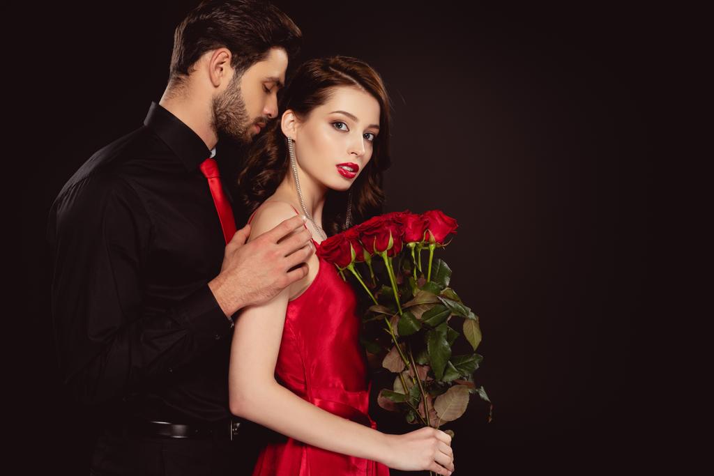 Side näkymä tyylikäs mies käsittää tyttöystävä punaisia ruusuja eristetty musta
 - Valokuva, kuva