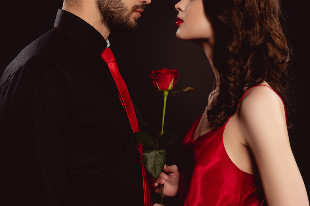 Vue recadrée de femme élégante tenant rose près du petit ami isolé sur noir
 - Photo, image