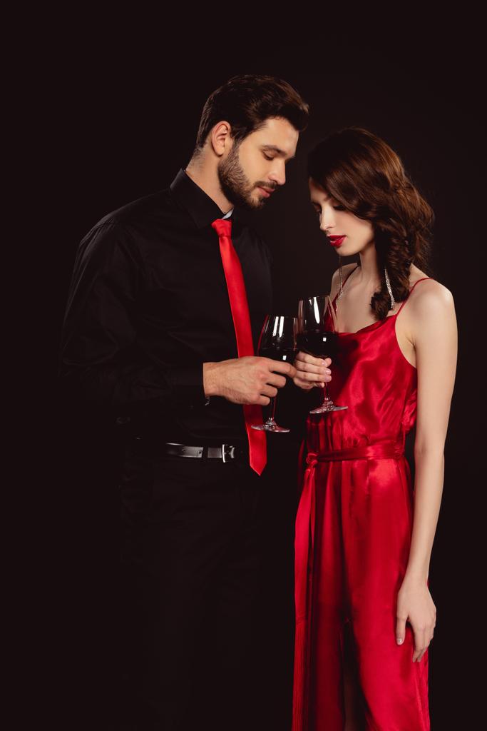 Seitenansicht eines eleganten Paares, das mit Rotwein auf Schwarz klirrt - Foto, Bild