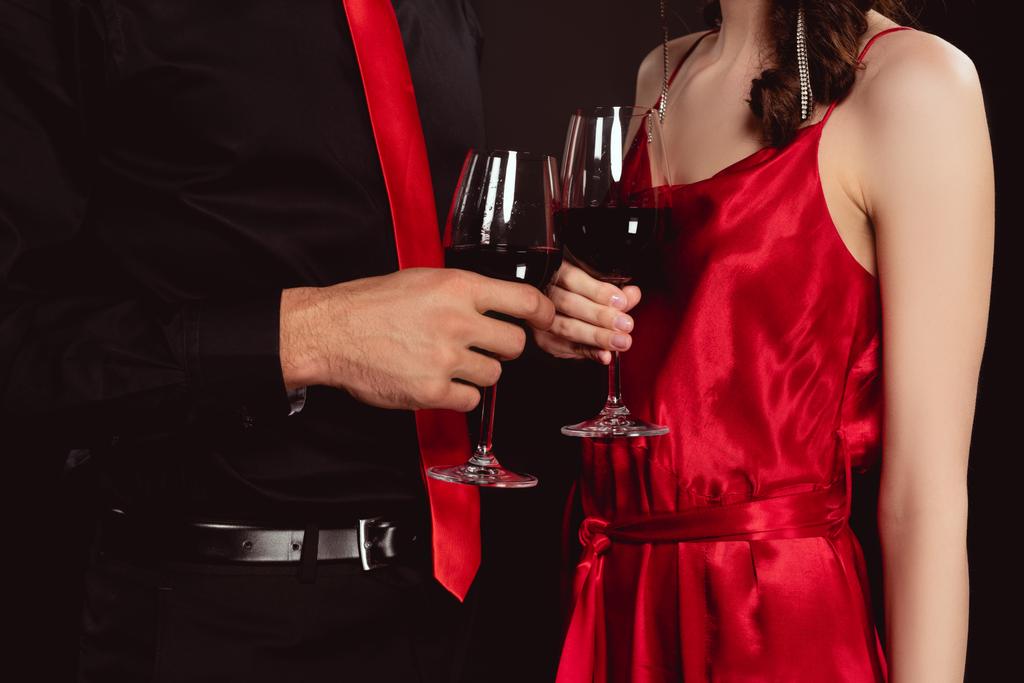 Vista recortada de pareja elegante tintineo con vino tinto aislado en negro
 - Foto, Imagen