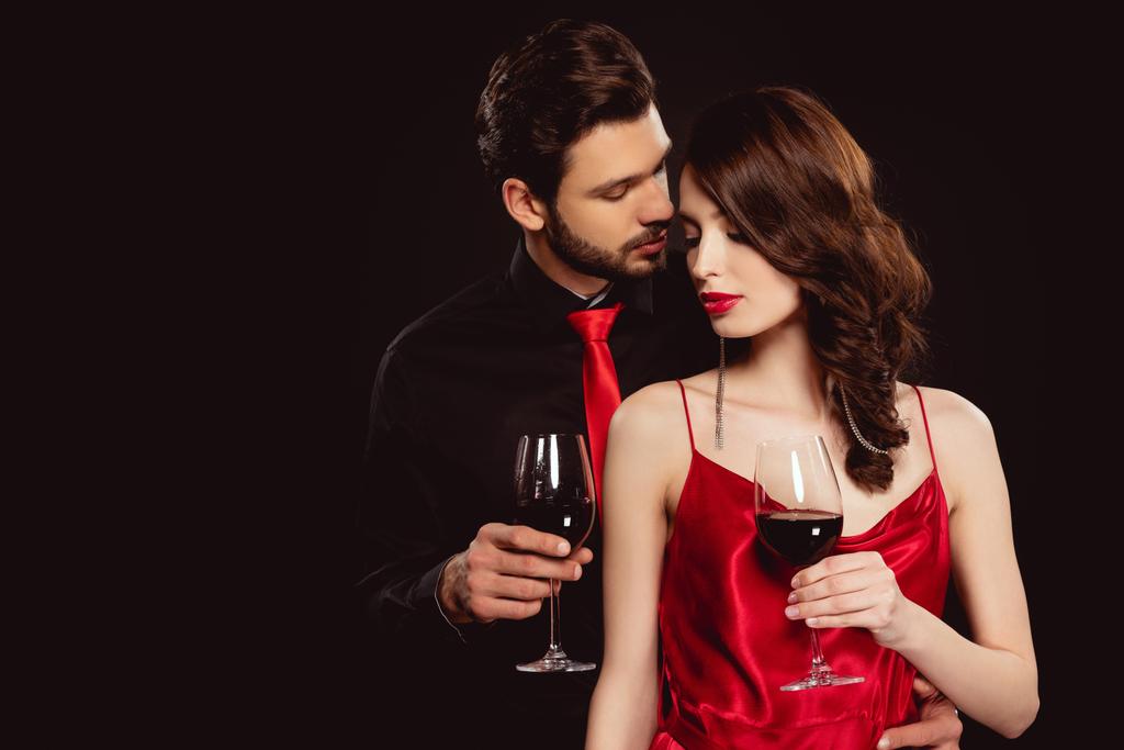 Elegáns férfi átöleli gyönyörű barátnő üveg vörösbor elszigetelt fekete - Fotó, kép