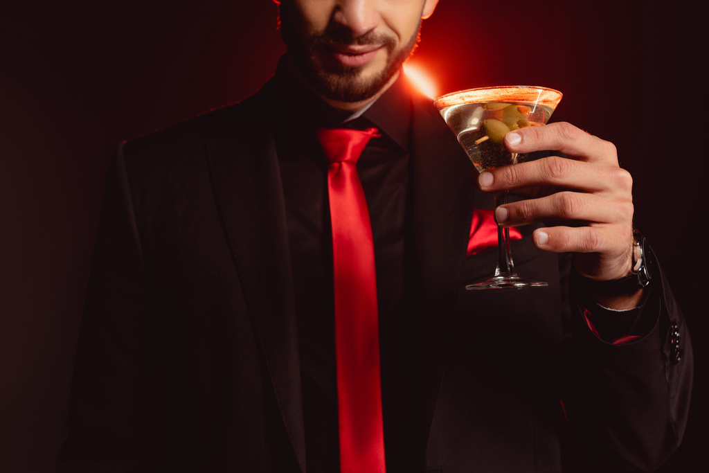 Rajatut näkymät tyylikäs mies tilalla lasi cocktail mustalla taustalla valaistus
 - Valokuva, kuva