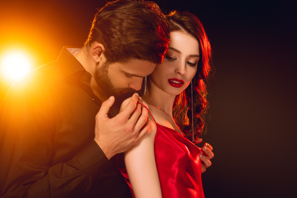 Side view of handsome man taking off dress from beautiful woman on black background with lighting - Photo, Image