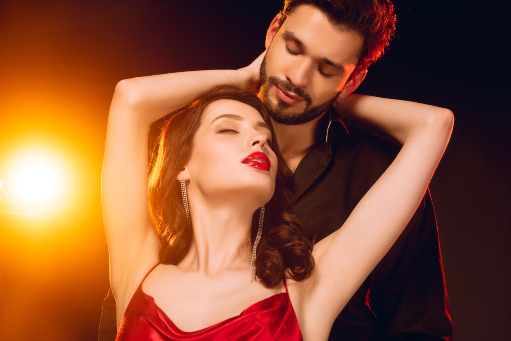 Elegant girl embracing handsome boyfriend on black background with lighting - Photo, Image