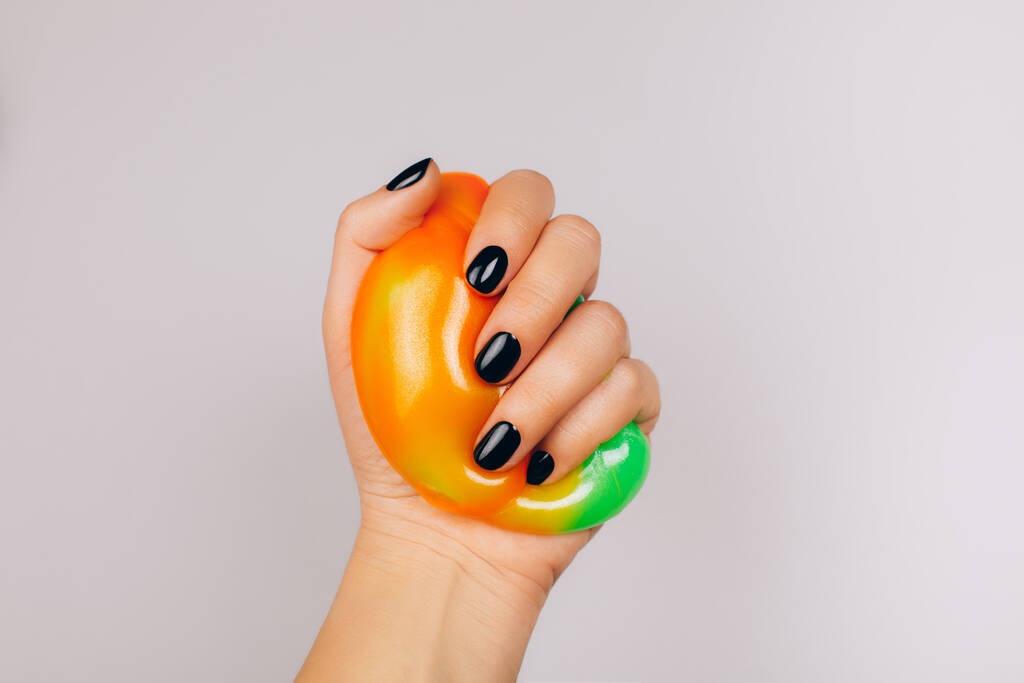 руки з чорним манікюром, що тримає слиз в помаранчевих і зелених яскравих кольорах
 - Фото, зображення