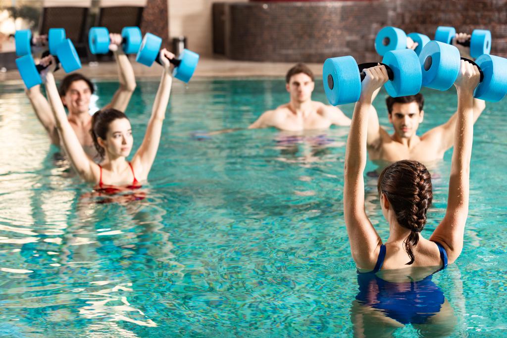 Selective focus of trainer holding barbells while exercising water aerobics with people in swimming pool - Photo, Image