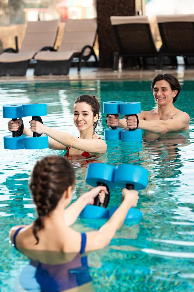 Selektywne skupienie się na uśmiechniętym mężczyźnie i kobiecie patrzących na trenera ze sztangą w basenie - Zdjęcie, obraz