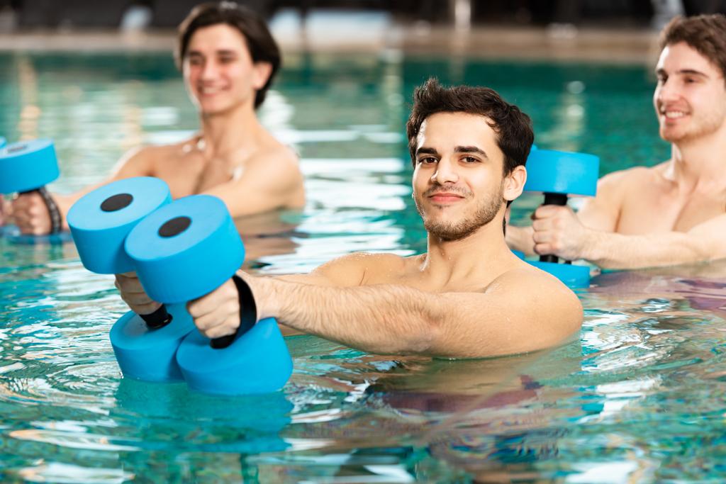 Focus selettivo dell'uomo con i bilancieri che sorridono alla telecamera mentre si esercita in piscina
 - Foto, immagini