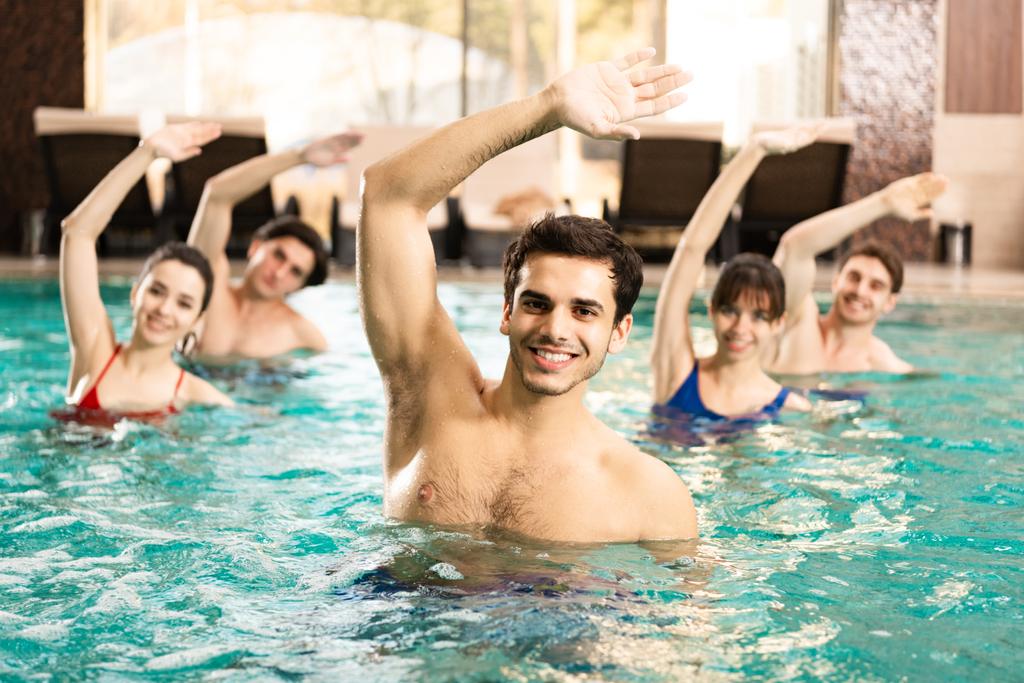 Selektywne skupienie przystojnego trenera uśmiechniętego do kamery podczas treningu z ludźmi w basenie - Zdjęcie, obraz