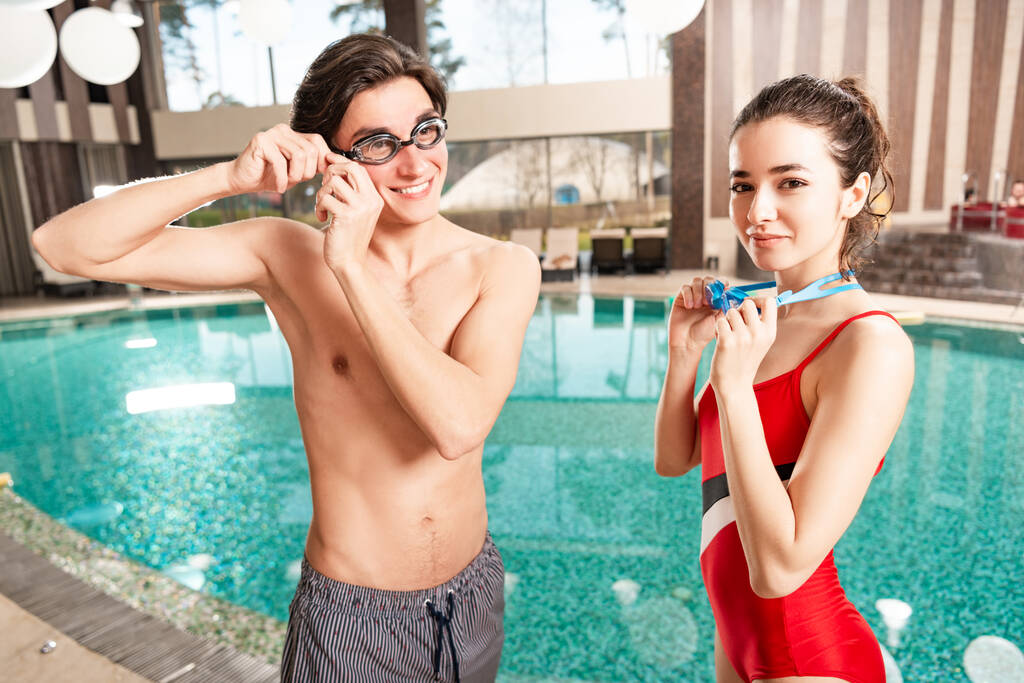 Χαμογελώντας άνδρας και γυναίκα κρατώντας googles κολύμπι κοντά στην πισίνα - Φωτογραφία, εικόνα