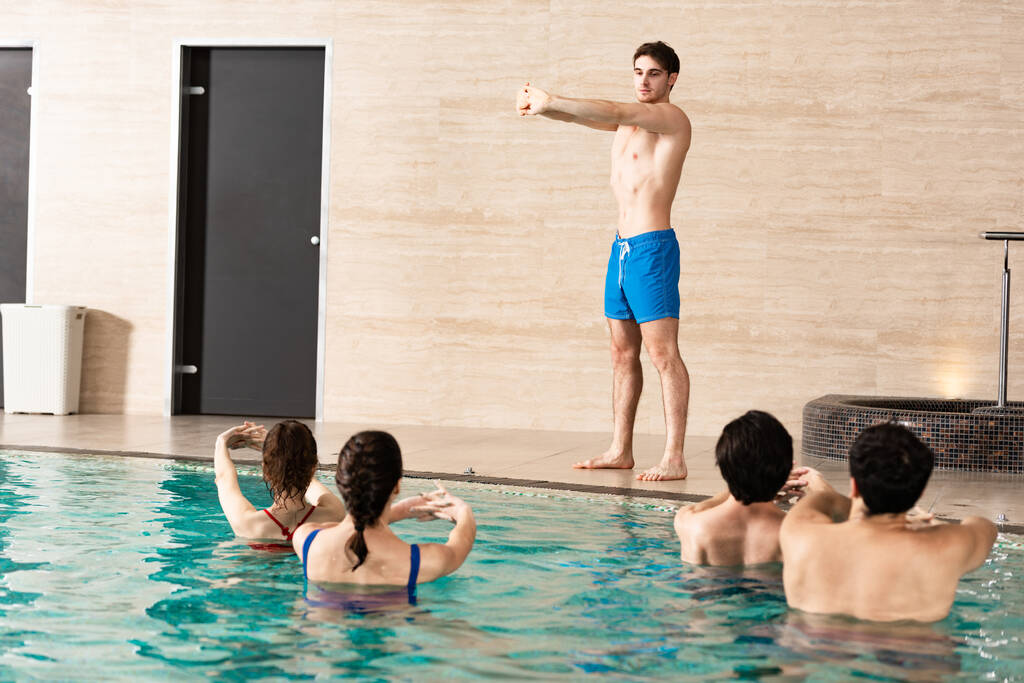 Guapo entrenador de ejercicios aeróbicos acuáticos con los jóvenes en la piscina
 - Foto, imagen