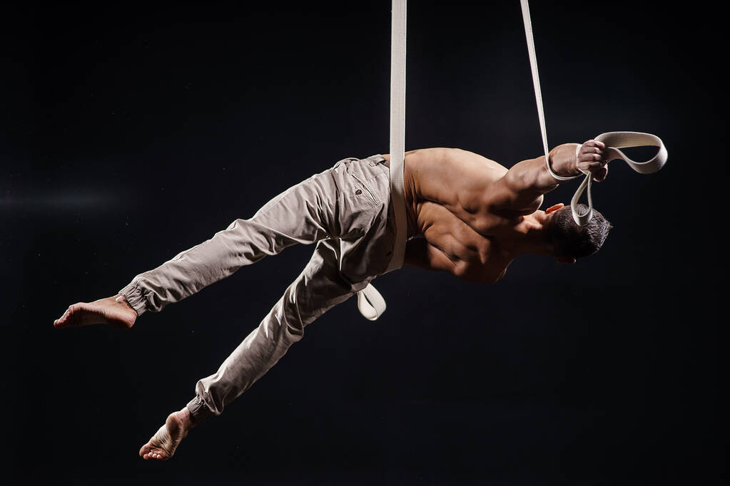 sirk sanatçısı hava kayışları ile güçlü üzerinde siyah arka plan üzerine kasları - Fotoğraf, Görsel