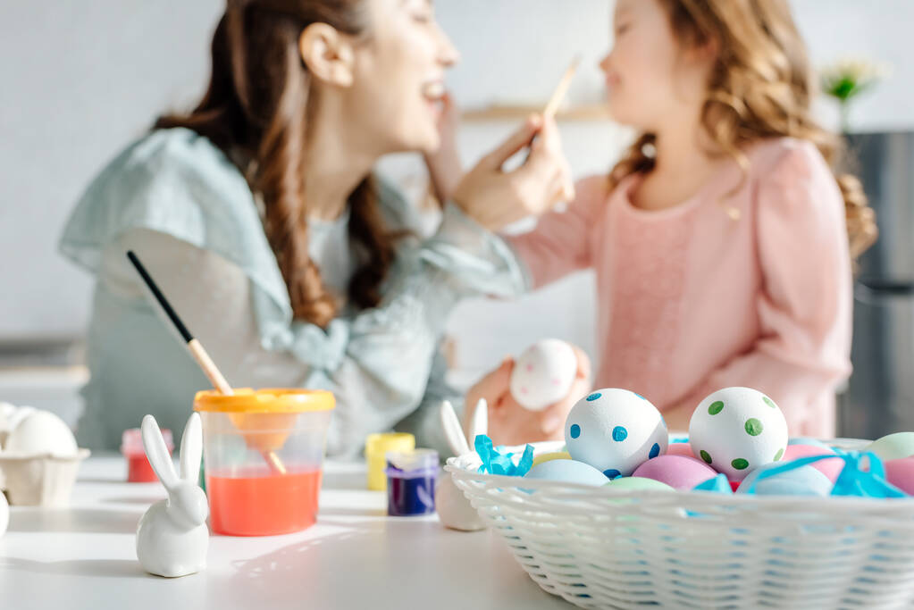 selective focus of painted easter eggs near decorative bunnies, happy mother and daughter  - Photo, Image