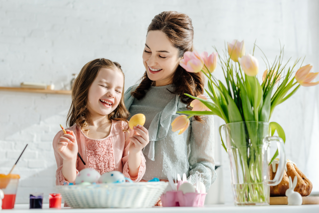 focalizzazione selettiva di madre e figlia felici vicino a tulipani, uova di pollo e pane pasquale
 - Foto, immagini