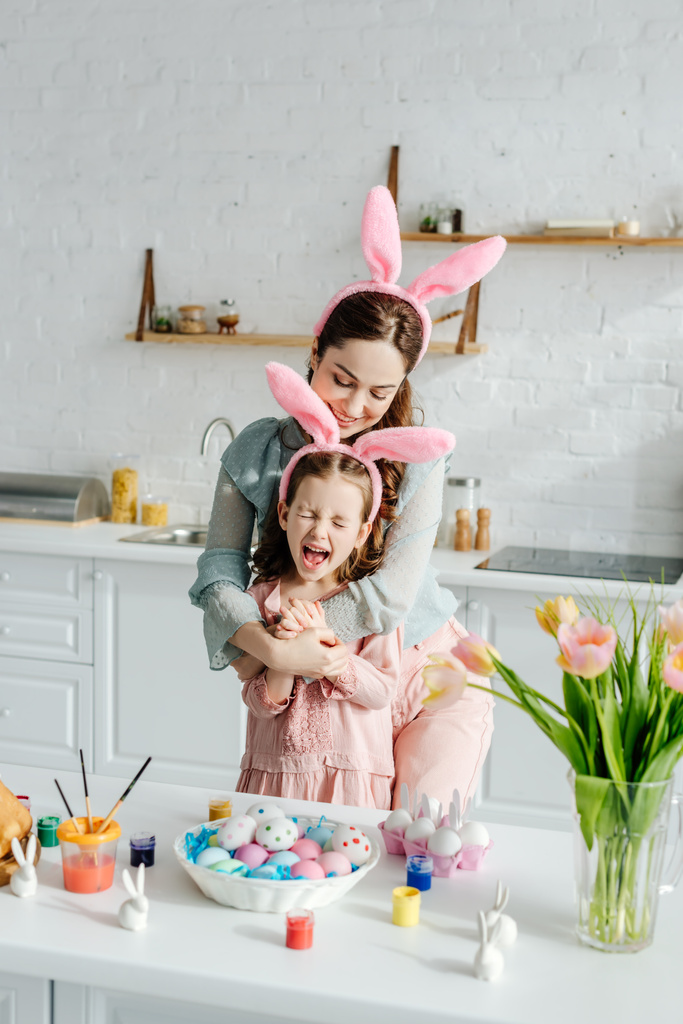 feliz madre abrazando excitado hija en conejito orejas cerca de Pascua huevos
  - Foto, imagen