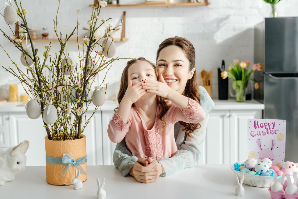 Çocuğun ağzı annesinin yanında, paskalya yumurtaları, söğüt ağacı ve dekoratif tavşanlar.  - Fotoğraf, Görsel