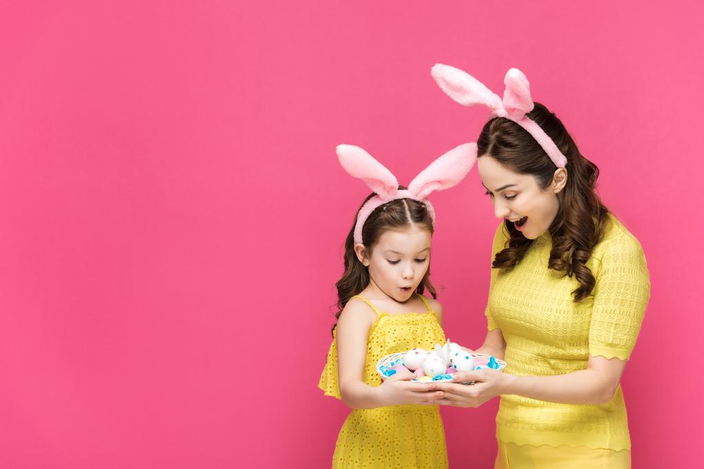 meglepett anya és lánya nyuszifül nézi húsvéti tojás elszigetelt rózsaszín  - Fotó, kép