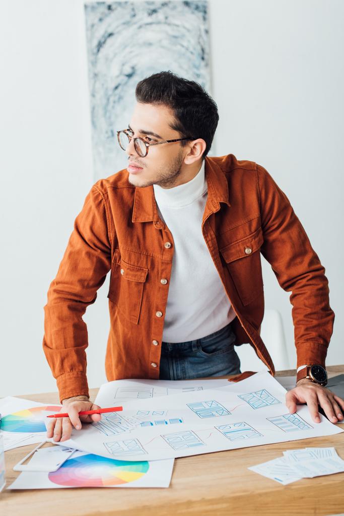 Handsome ux designer looking away while working with website templates on table - Photo, Image