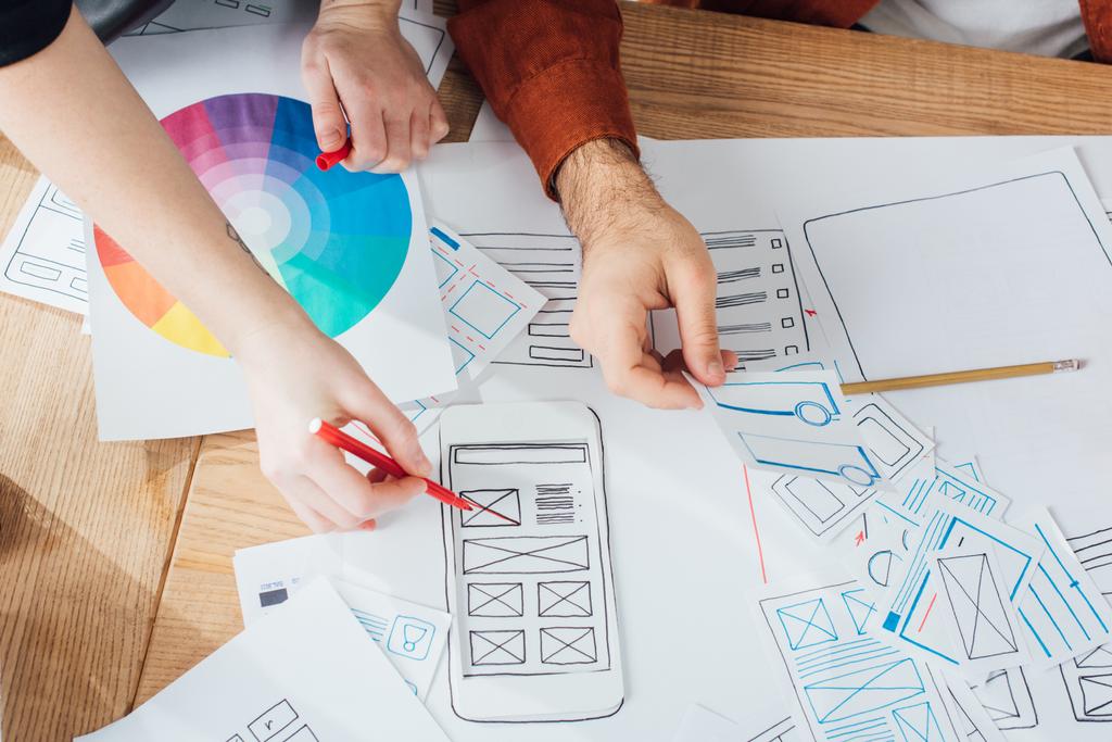 Обрізаний вид дизайнерів, які планують дизайн користувача з розкладками та кольоровим колом на столі
 - Фото, зображення
