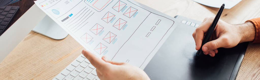 Обрезанный вид дизайнера планирования пользовательского опыта проектирования сайта и использование графического планшета за столом, панорамный снимок
 - Фото, изображение