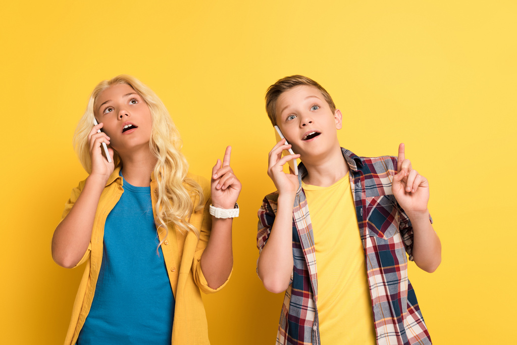 мечтательные дети, показывающие идеи жест и говорить на смартфонах на желтом фоне
  - Фото, изображение