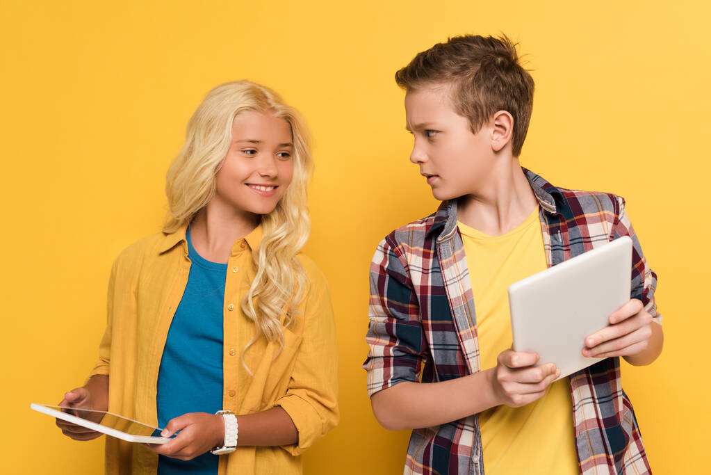 uśmiechnięty dzieciak patrząc na cyfrową tabliczkę swojego przyjaciela na żółtym tle  - Zdjęcie, obraz