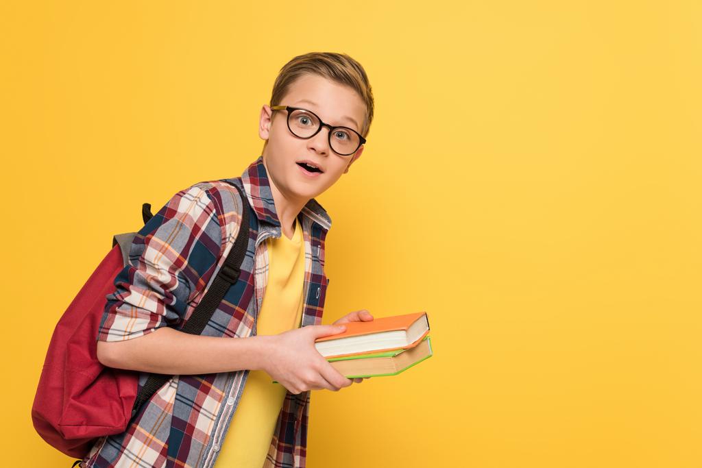 šokovaný školák s brýlemi drží knihy izolované na žluté - Fotografie, Obrázek