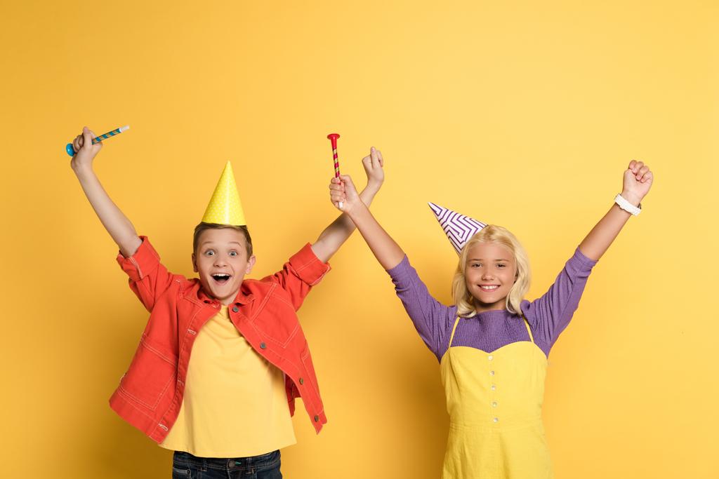 smiling kids with outstretched hands holding party horns on yellow background  - Photo, Image