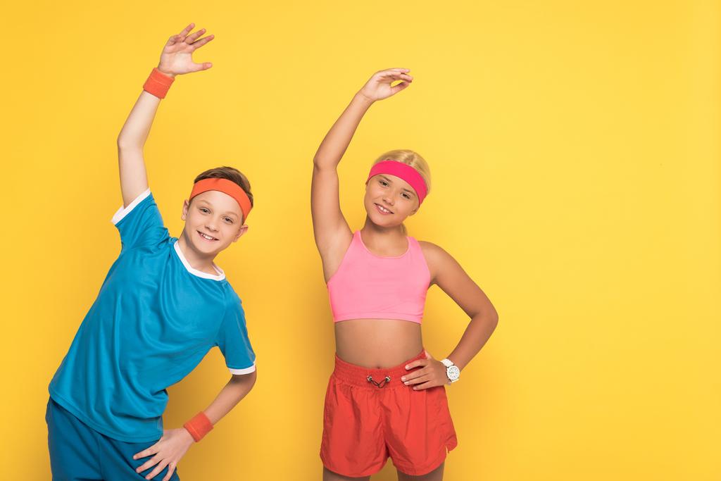 Lächelnde Kinder in Sportbekleidung beim Training und beim Blick in die Kamera auf gelbem Hintergrund  - Foto, Bild