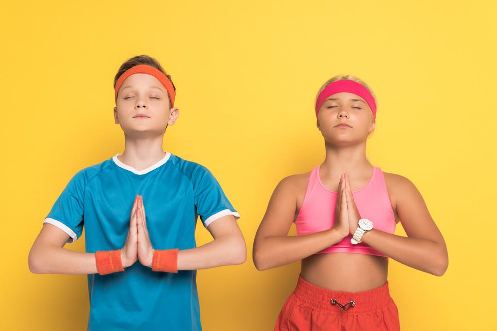 lapset urheiluvaatteet suljetuin silmin osoittaa rukoilevat kädet keltaisella taustalla
  - Valokuva, kuva